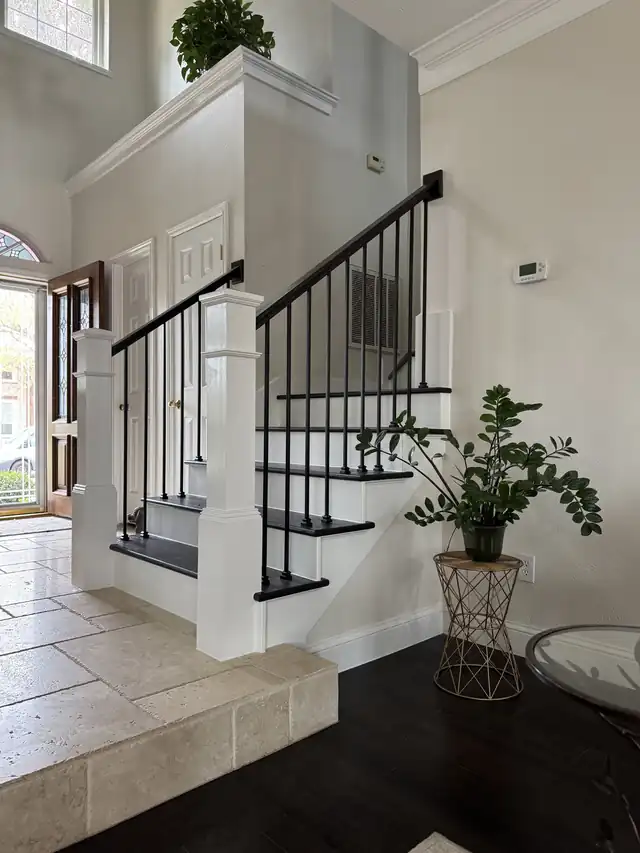 Black iron stair balusters with a white box newel in a tiled foyer
