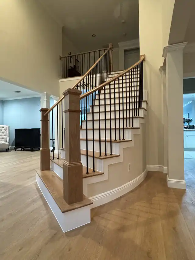 Curved oak staircase with black iron balusters and a stained box newel