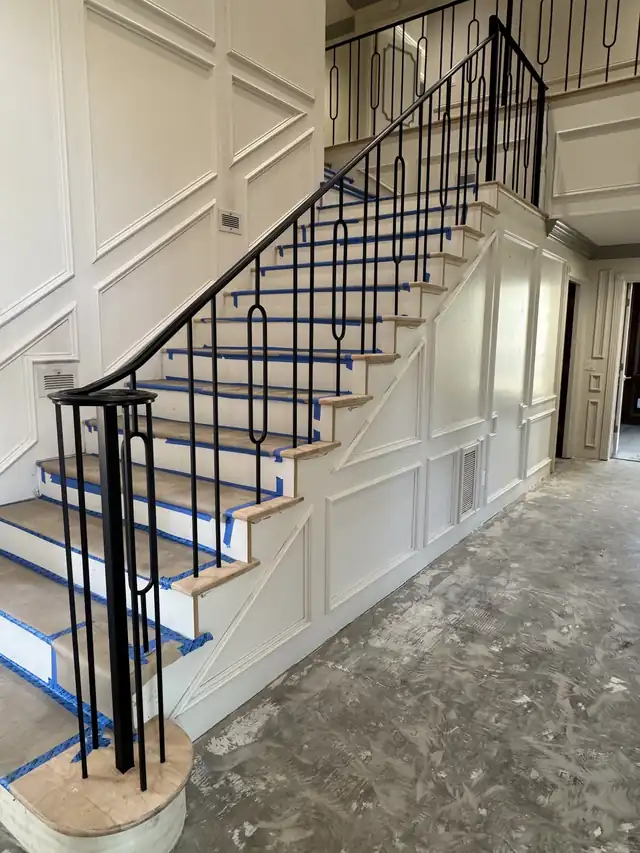Staircase mid-job with new iron balusters set along a wainscot wall