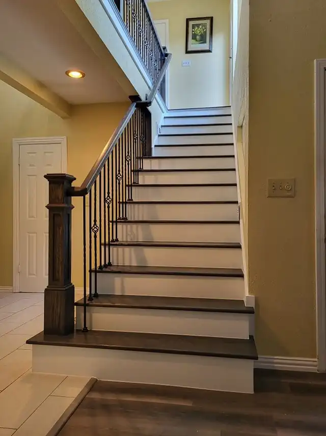 Straight staircase with black iron balusters, a dark newel and stained treads