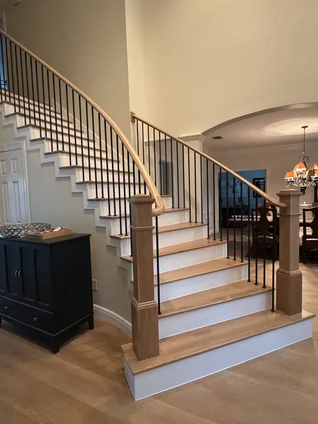 Sweeping curved stair with an oak handrail, black iron balusters and white risers