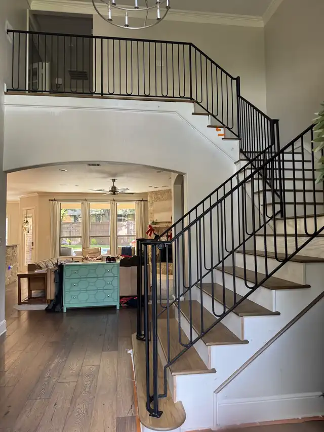 Curved stair with a black iron rail sweeping down toward an arched kitchen